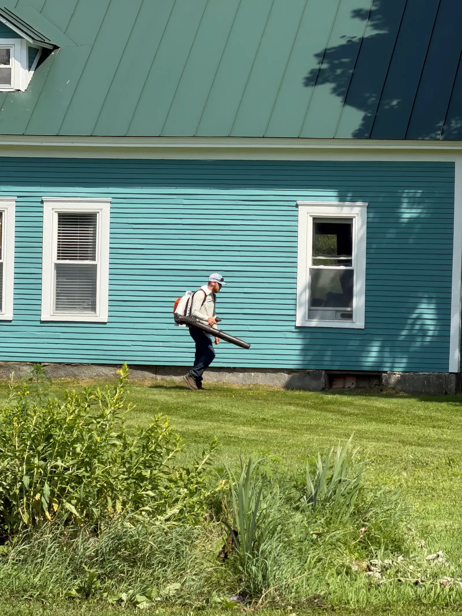 Blowing clippings off the foundation of a teal farmhouse