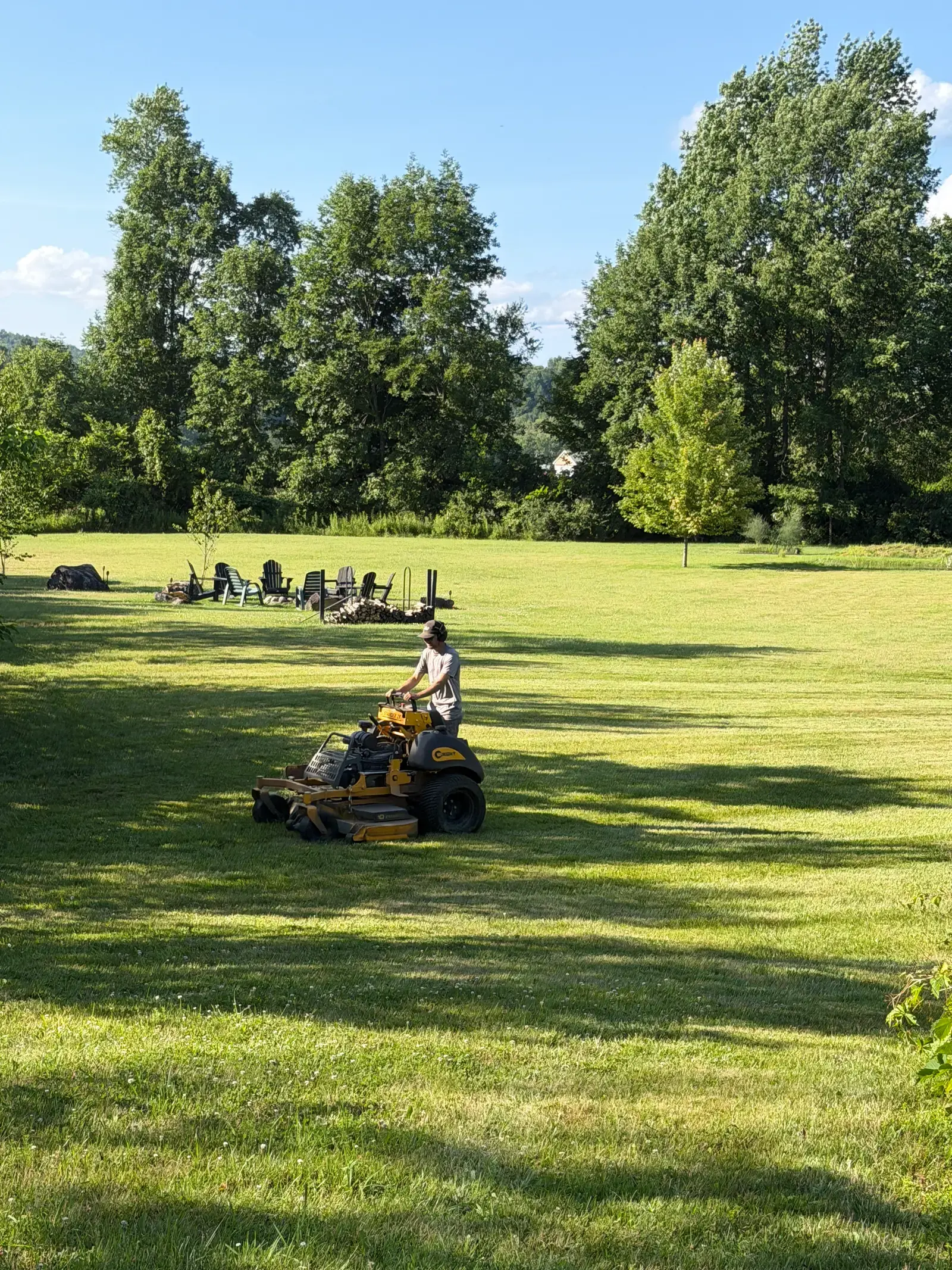 Stand-on mower cutting a wide open lawn beside a treeline