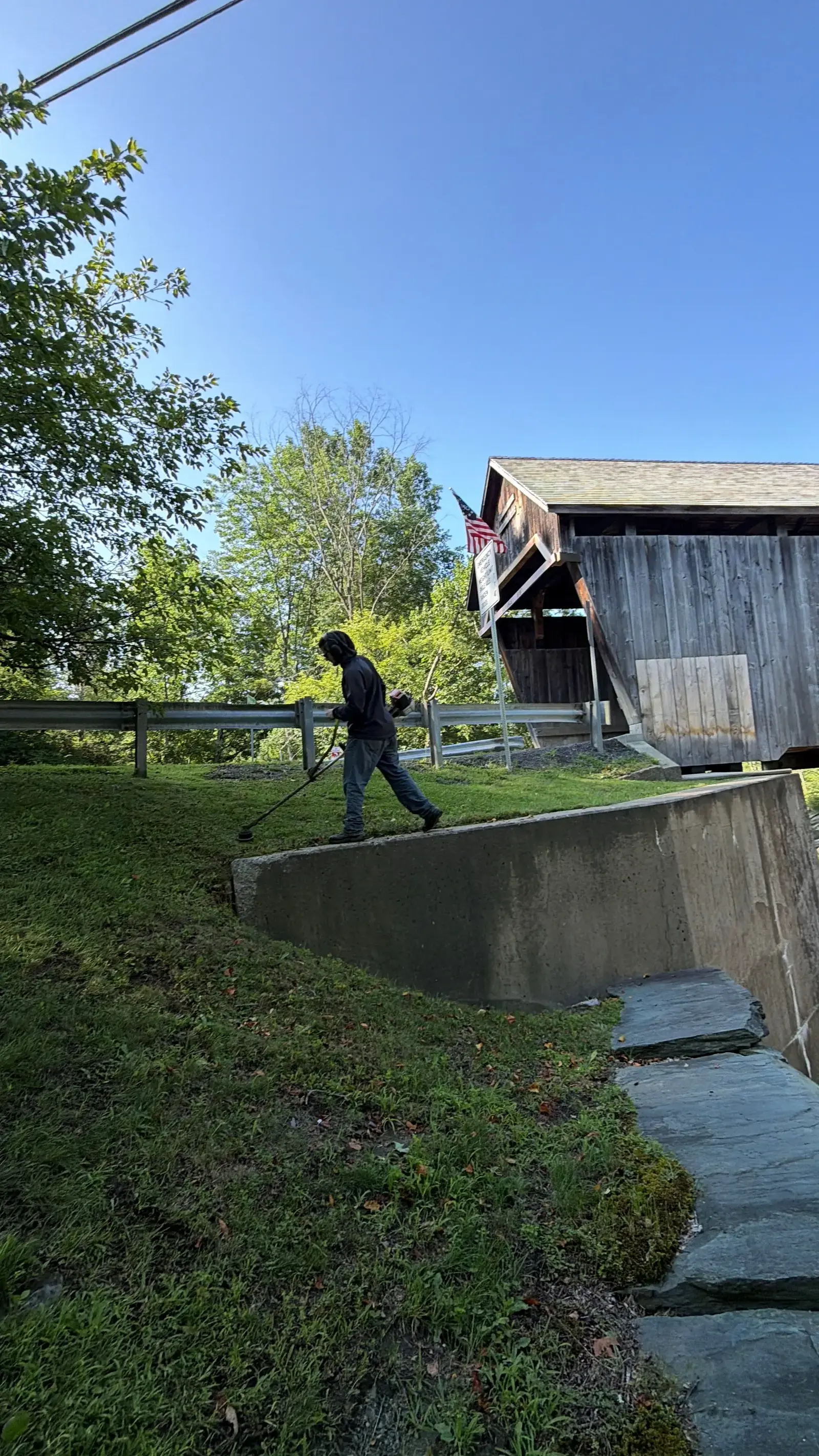 Crew member trimming the bank beside a Vermont covered bridge