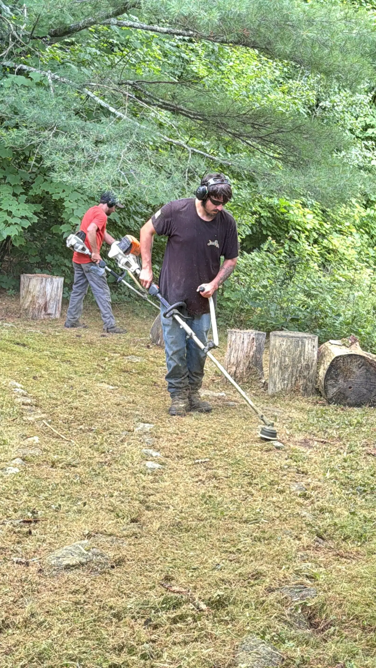 Two Eagle Lawn crew members trimming a wooded property line